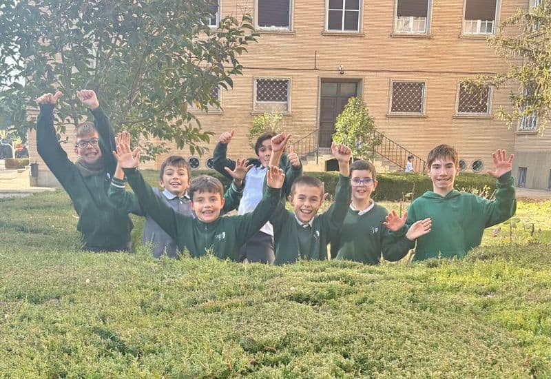 Alumnos de primaria saludando a cámara de forma animada durante su descanso en el patio del colegio en un ambiente de convivencia positiva.