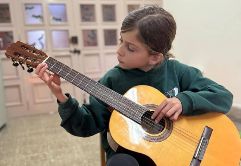 Alumna de Primaria concentrada tocando la guitarra española, como ejemplo de la educación práctica e individualizada en la Escuela de Música San Gabriel.