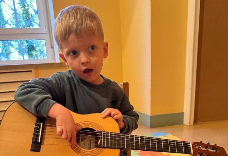 Niño de la etapa de Infantil interactuando con una guitarra española grande, reflejando el fomento de la curiosidad y la creatividad musical desde edades tempranas.