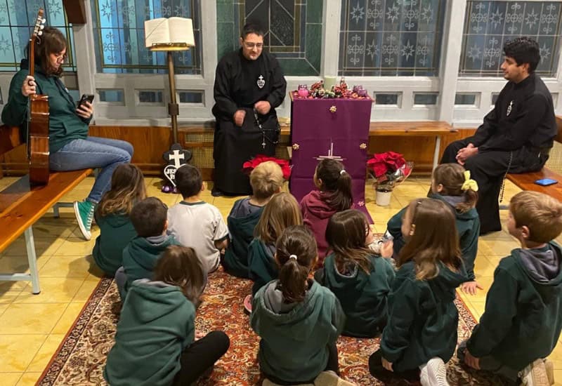 Alumnos de primaria participando en un taller de pastoral y educación en valores junto a un sacerdote en el oratorio del centro.