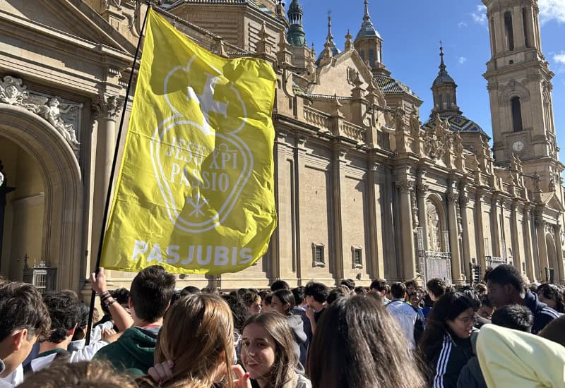 Bandera corporativa del Colegio San Gabriel de Zuera situada frente a las torres de la Basílica del Pilar en Zaragoza durante una actividad escolar.