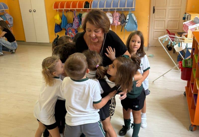 Profesora de Educación Infantil abrazando a un grupo de alumnos en el aula del Colegio San Gabriel.