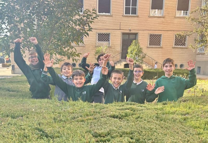 Alumnos de Primaria del Colegio San Gabriel sonriendo y saludando en los jardines de las instalaciones del centro.